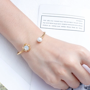Detail shot of open gold bracelet featuring opal-like flower and elegant white pearl
