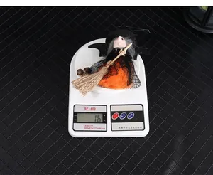 Close-up of a lightweight Halloween witch doll with broom on a scale showing 16 grams
