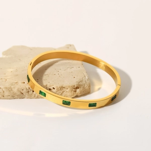 Detail of gold titanium steel bangle featuring a rectangle green zircon on a stone surface