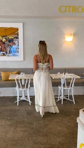 Detail of white maxi dress with black piping trim and back cutout in a restaurant setting