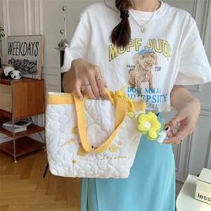 Detail of white quilted tote bag featuring yellow straps and floral sun pendant accessory