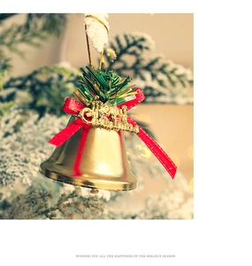 Macro view of gold Christmas bells with red bow and Merry Christmas text on pine branches