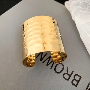 Detail of wide golden cuff bracelet featuring a unique hammered metal texture finish