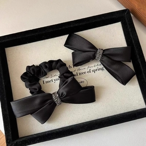 Close-up of black satin bow hair clip and scrunchie set with sparkling rhinestone centers