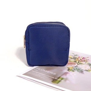 Detail of a dark blue nylon cosmetic pouch with a gold zipper on a decorative magazine