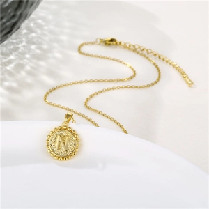 Detail shot of golden circular letter N pendant with beaded edge on a thin chain