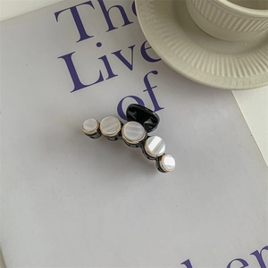Detail of a black hair claw clip featuring five round white stones in gold metal frames