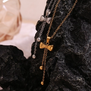 Detail of bow-shaped tassel necklaces in gold and silver finish on a dark stone background