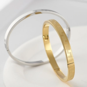 Macro detail of gold and silver steel bracelets with geometric etched Greek key pattern