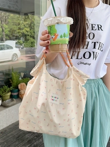 Beige canvas tote bag with pink bear and bow patterns shown in a lifestyle outdoor setting