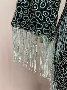 Detail of silver sequins and long tassels on black dress sleeve with shimmering texture