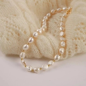 Detailed close-up of Baroque pearl necklace with gold beads on beige lace fabric