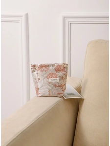 Portable floral embroidery cosmetic bag with gold petal zipper on beige sofa