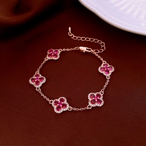 Détail d'un bracelet trèfle en or rose avec pierres rouges sur fond de velours