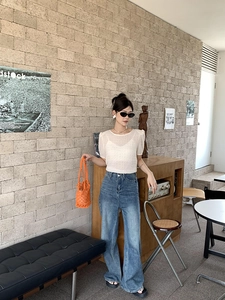 Fashionable outfit featuring a white knit top, blue wide-leg jeans, and an orange woven bag