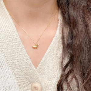 Detailed view of a golden whale pendant necklace worn with a white knit cardigan