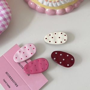 Close-up of four-piece polka dot hair clip set in red and cream on aesthetic fabric