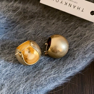 Detailed view of elegant gold spherical hoop earrings on a plush grey texture background