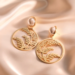 Gold leaf drop earrings with pearl studs displayed on beige silk fabric background