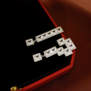 Macro detail of asymmetric silver earrings with square-cut zircons on a luxury red box