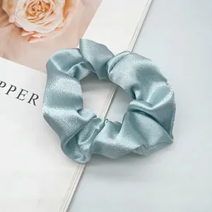 Detailed view of light blue satin scrunchie with silky texture and elegant folds