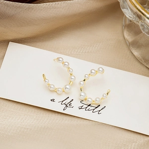 Detail of C-shaped gold pearl earrings on elegant silk background with lifestyle card