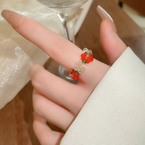 Close-up of handmade red and white beaded flower ring on model's finger with soft lighting