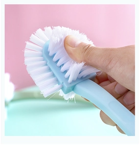 Close-up of a blue plastic shoe brush with dense white nylon bristles held by a hand