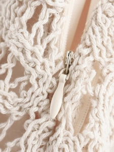 Gros plan sur la texture du tricot blanc et le détail de la fermeture éclair en goutte