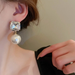 Elegant silver earrings with square-cut crystal and large white pearl worn by a model