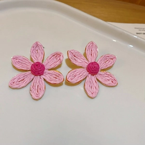 Detail shot of pink floral tassel earrings with straw texture and gold trim in a tray