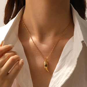 Detail of gold-plated horn pendant with dark gemstone on a delicate beaded chain