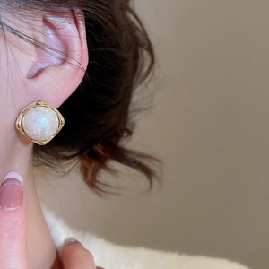 Close-up of elegant gold square earrings with white pearl inlay worn by a female model
