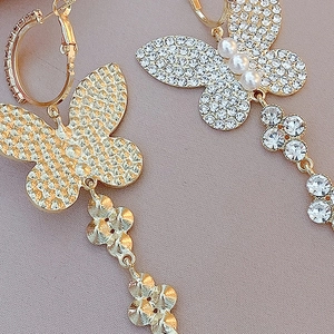 Detail view of asymmetric butterfly earrings with rhinestones, pearls and gold finish
