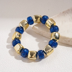 Macro shot of geometric acrylic beaded bracelet with blue starburst and gold cube beads