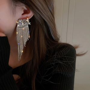 Close-up of sparkling rhinestone flower tassel earrings worn by a model in black
