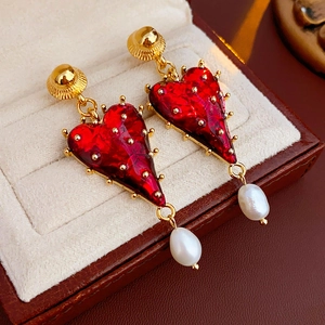 Detailed macro view of red heart earrings with gold trim and white dangling pearls