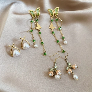 Detailed set of floral pearl earrings with butterfly tassels on champagne satin background