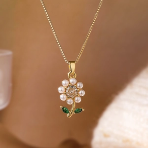 Detailed macro view of a gold flower pendant with pearl petals and green gemstone leaves