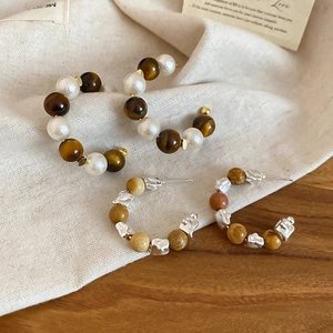 Détail de boucles d'oreilles créoles en œil de tigre et perles sur lin et bois naturel