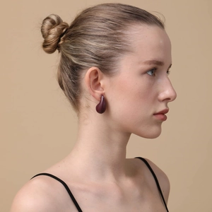 Detail view of smooth deep red water-drop stud earrings worn by a model in soft lighting