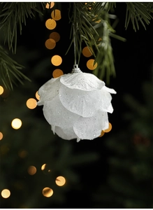 Macro view of white petal Christmas ball with glitter on a blurred festive tree branch