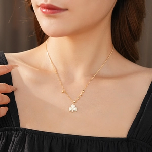 Close-up of a gold clover pendant necklace with white inlay on a female model
