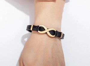 Detail of black leather braided bracelet featuring a golden infinity symbol and clasp
