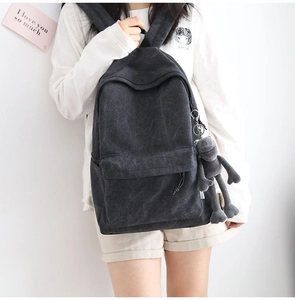 Detail of a dark grey canvas backpack with front zipper pocket and plush monkey charm