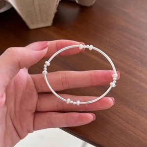 Detail shot of a minimalist S925 silver bracelet with small white pearls on a hand