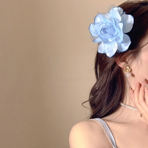 Detail of a large blue fabric flower hair clip worn by a model with elegant jewelry