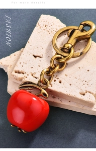 Detail of red apple keychain with vintage gold metal chain on a beige stone surface