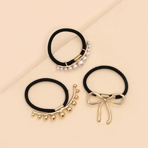 Detailed view of three black elastic hair ties with gold metal and white pearl accents