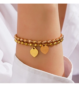 Detail of double-layer beaded bracelet with engraved gold heart charms on woman's wrist